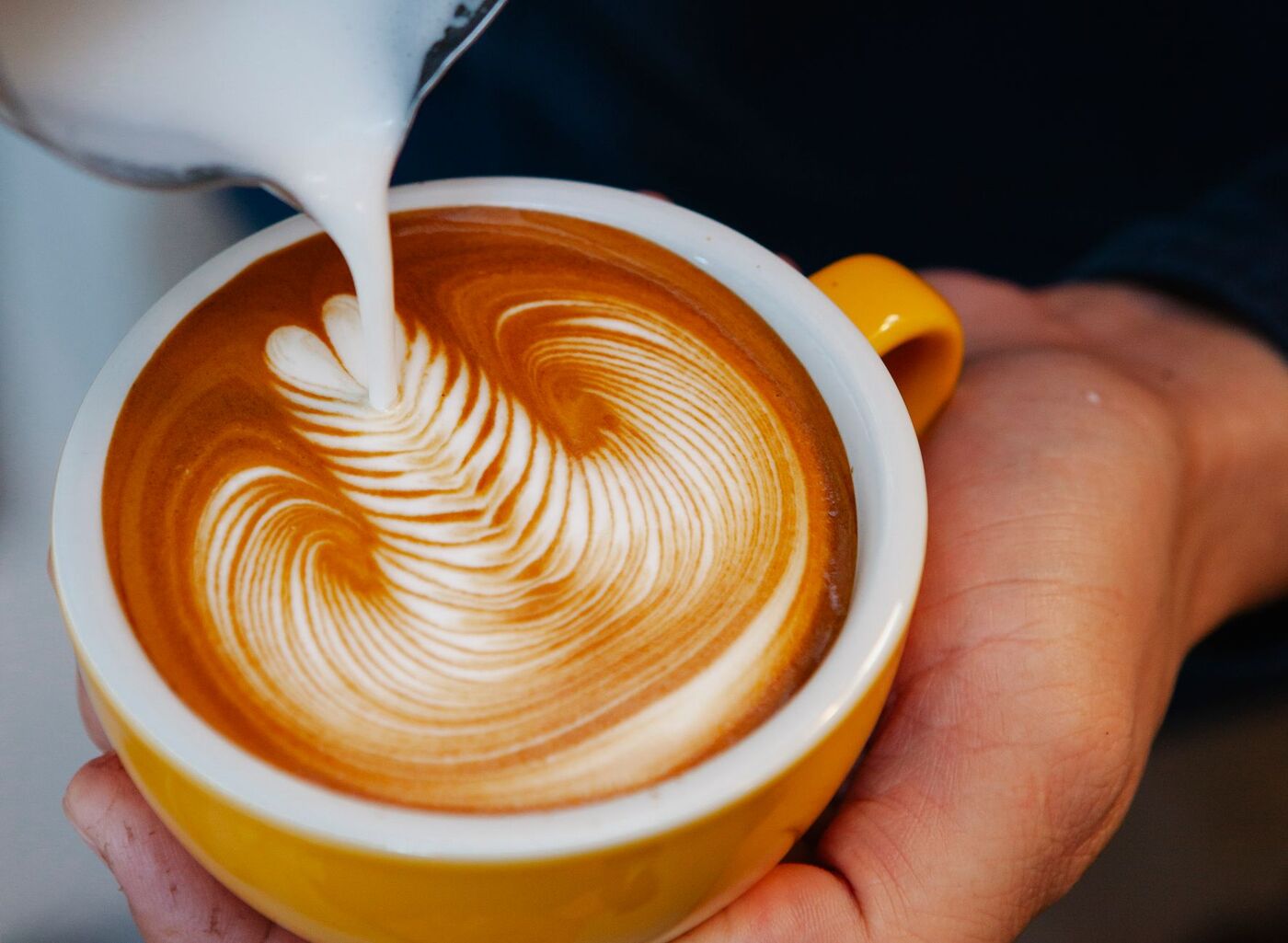 Barista häller latte art i en gul kopp på ett Stockholmskafé