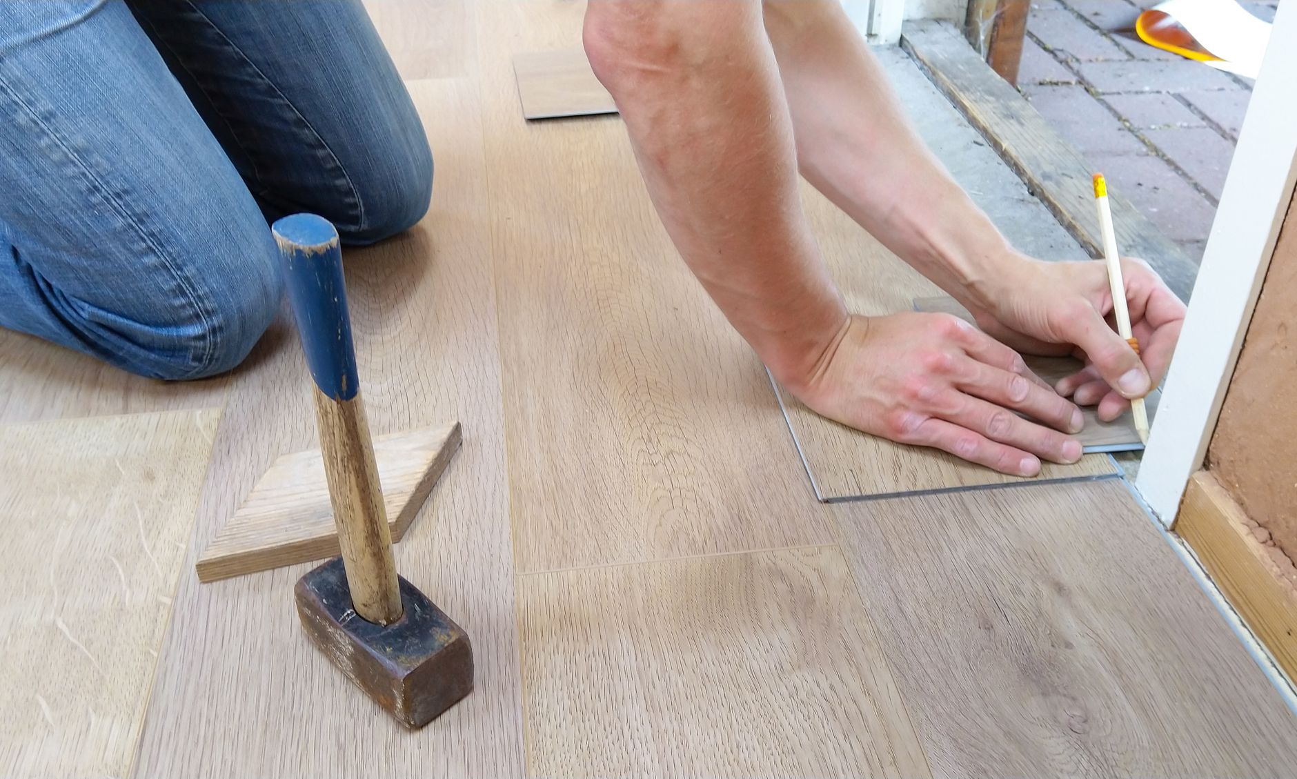 Hantverkare mäter och kapar golvbräda vid dörröppning under installation
