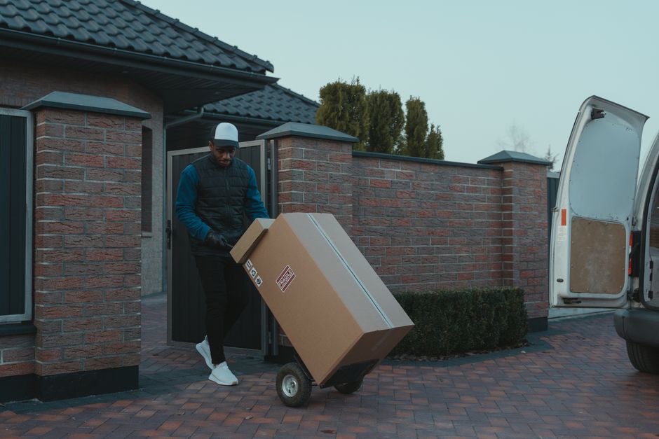 Flyttgubbe kör en kärra med flyttkartonger till flyttbilen utanför en villa i Stockholm