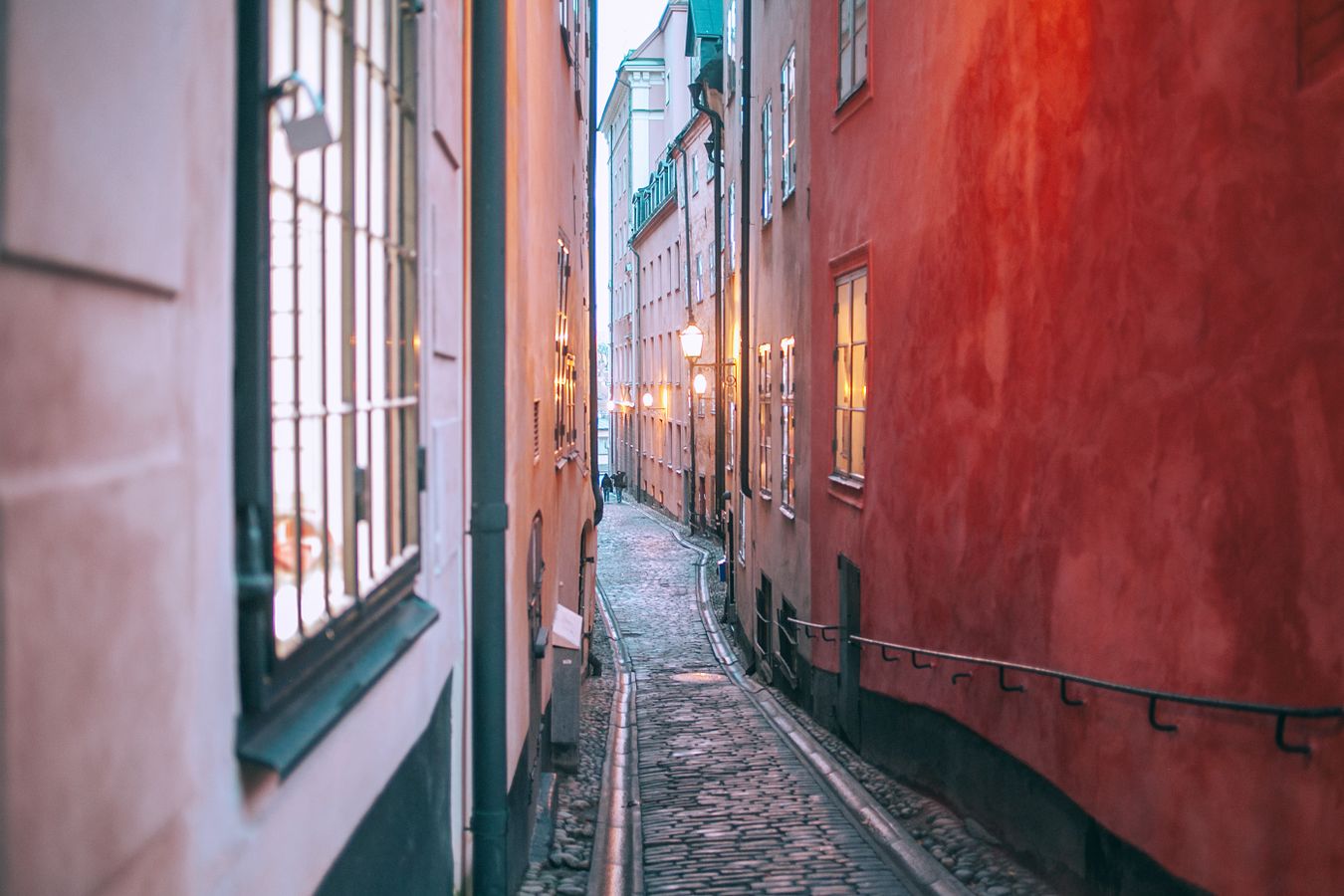 Smal historisk gränd i Gamla Stan med tända gatlyktor i skymningen, typisk för områdets medeltida gatunät